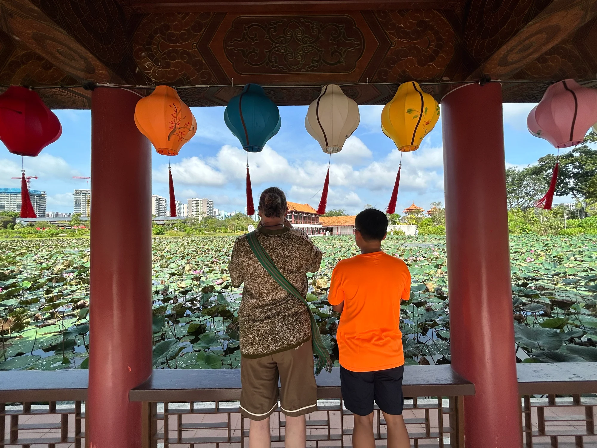 Tour guide and guest looking over the lotus pond from a lantern-lit pavilion in the Chinese Garden